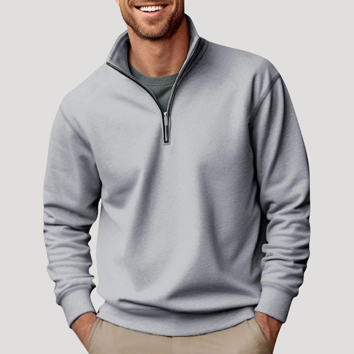 Man wearing a light grey, soft-fabric quarter-zip sweatshirt with a funnel neck and relaxed fit over a dark t-shirt.