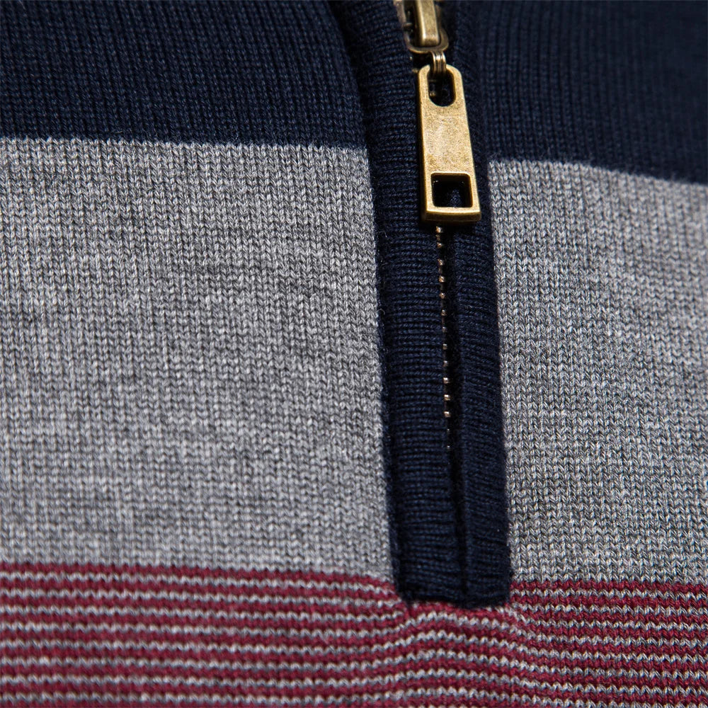 Close-up of a navy, grey, and burgundy striped knit jumper featuring a brass-toned quarter-zip neckline.