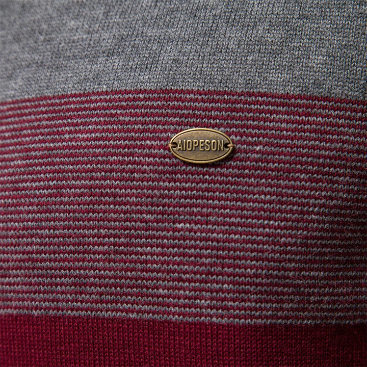 Close-up of a grey and burgundy striped knit jumper with a metallic Aiopeson brand logo badge.