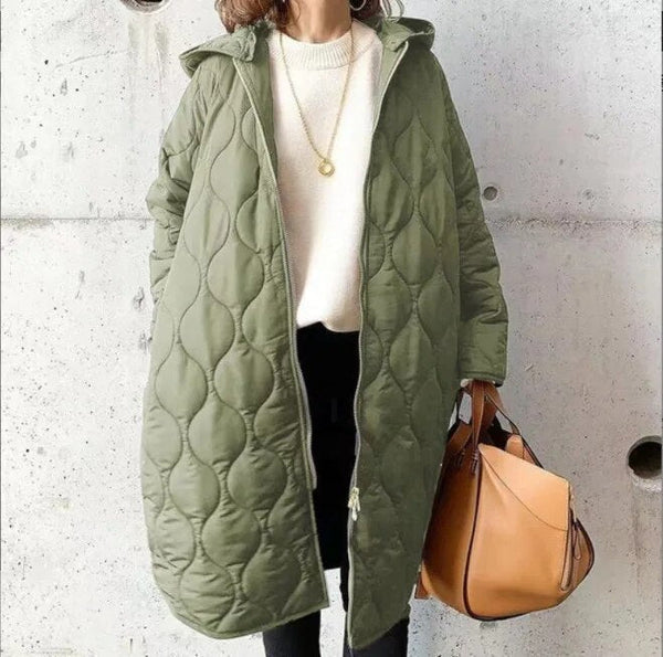 Olive green longline quilted coat with a hooded, relaxed silhouette and full-length zip, worn over a white knit sweater.