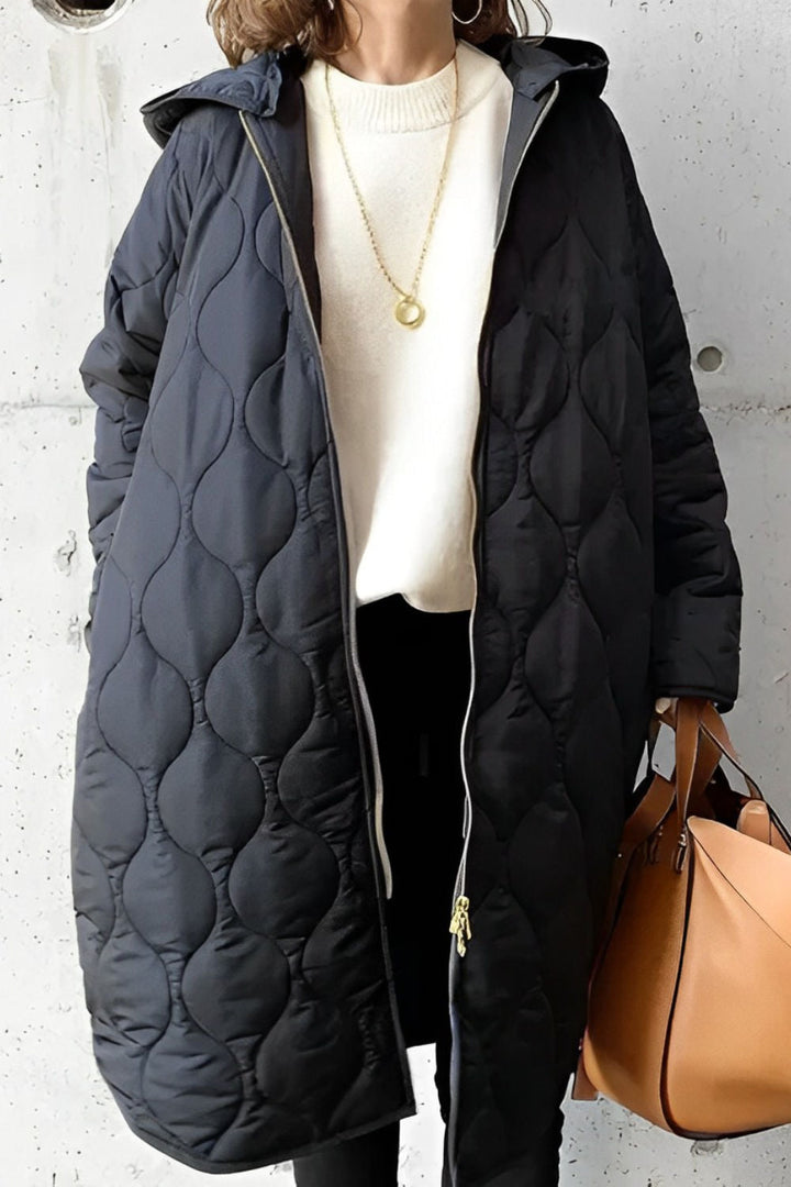 Black longline onion-quilted hooded coat with a full-length zip, worn over a white knit sweater.