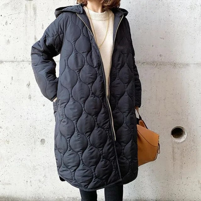 Black longline hooded coat with onion-quilted padding, full-length zip, and a relaxed fit worn over a cream sweater.