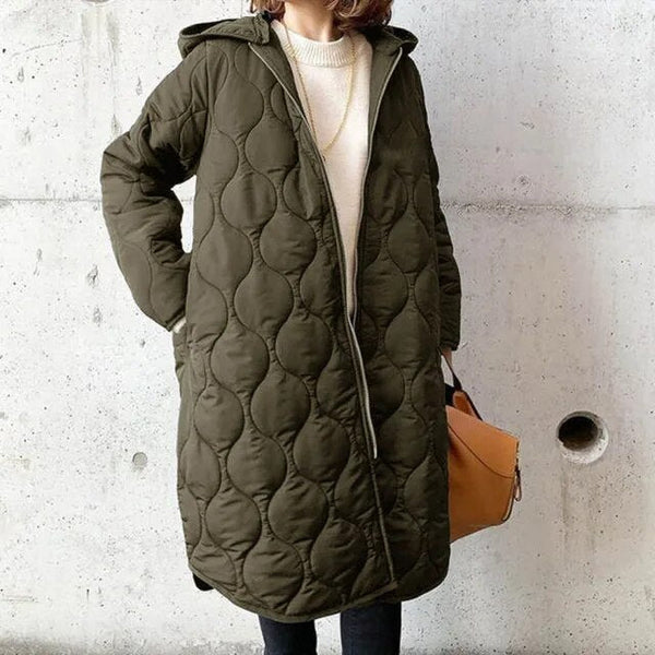 Olive green longline quilted coat with a hooded design, full-length zip, and relaxed fit worn over a cream sweater.