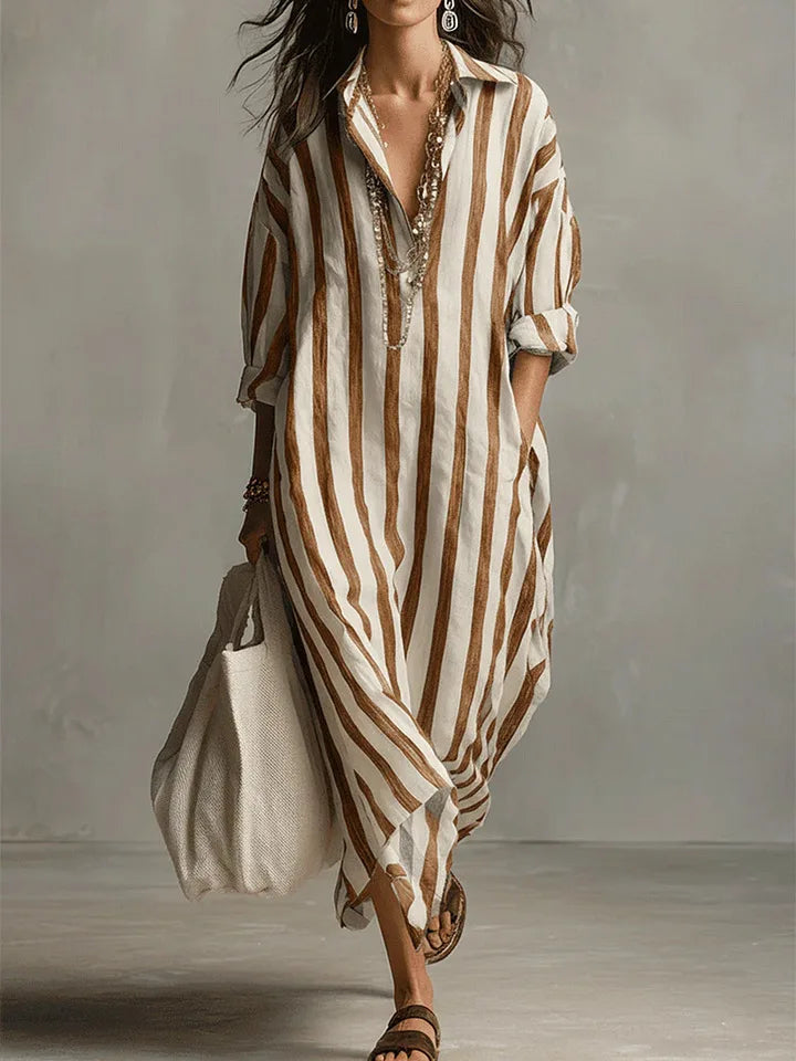 Woman wearing a loose, brown and white striped linen maxi shirt dress with an open collar and long sleeves.