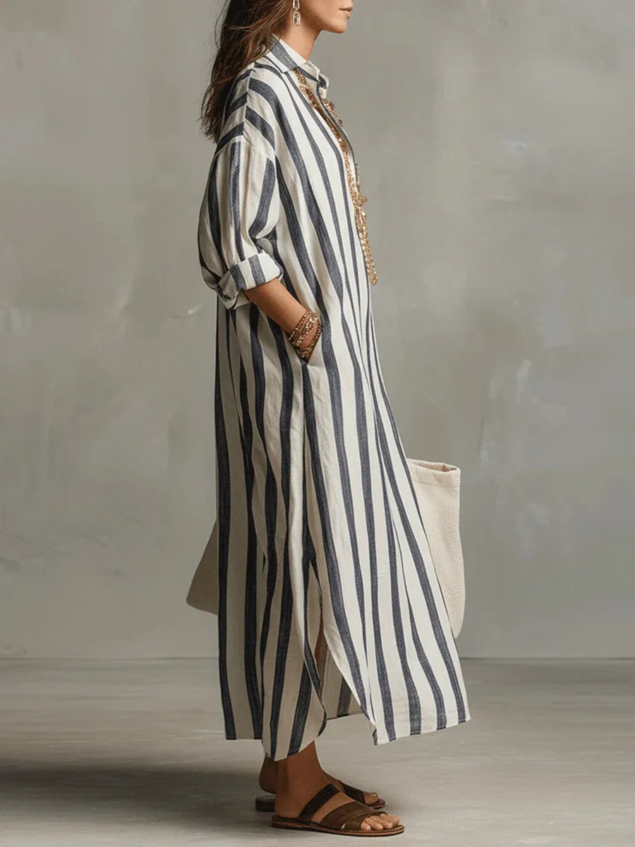 Woman wearing a loose, striped linen maxi shirt dress with a collar, side slits, and rolled sleeves.