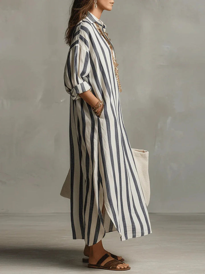 Woman wearing a loose, striped linen maxi shirt dress with a collar, side slits, and rolled sleeves.