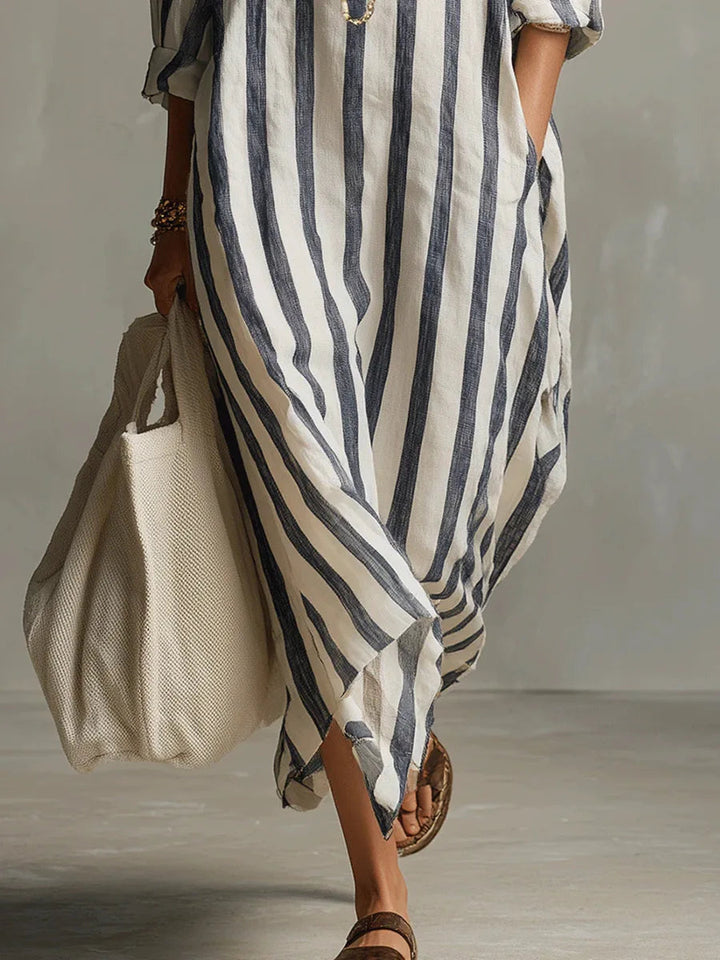 Woman wearing a breezy, loose-fit maxi shirt dress in white and navy blue vertical stripes, paired with a large tote bag.