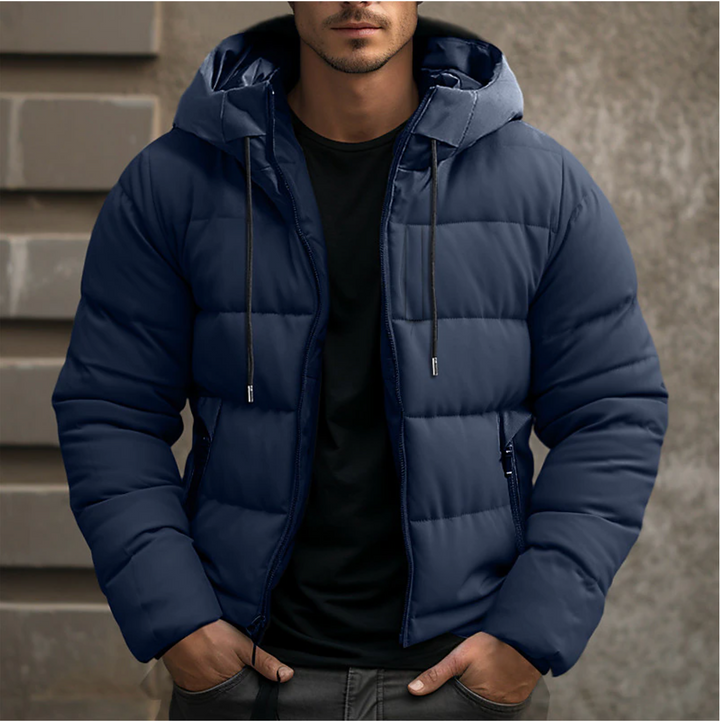 Navy blue men's hooded puffer jacket with quilted insulation, full-length zip, and drawstring hood over a black t-shirt.
