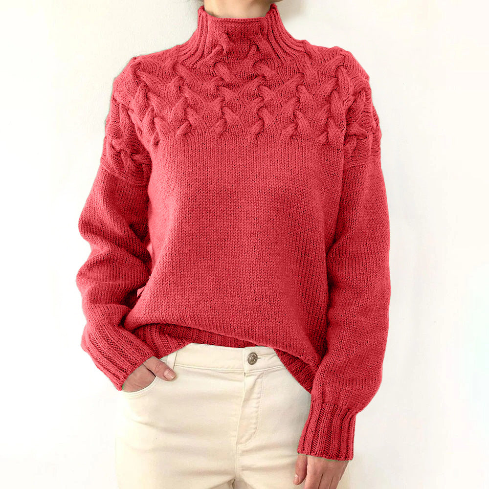 Red cable knit turtleneck jumper with a braided yoke design, relaxed fit, and ribbed cuffs worn with cream trousers.