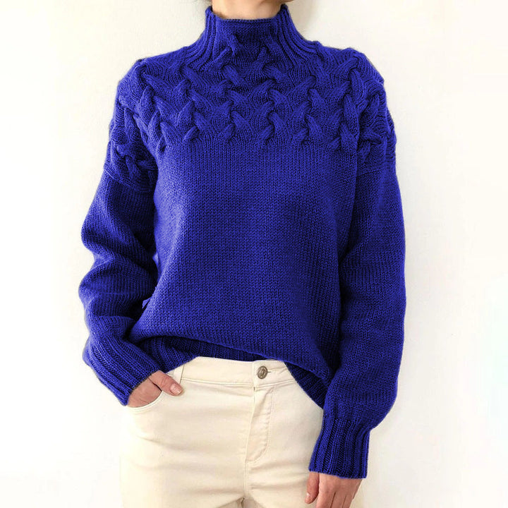 Royal blue cable-knit turtleneck jumper with a braided yoke, relaxed fit, and ribbed cuffs paired with cream trousers.