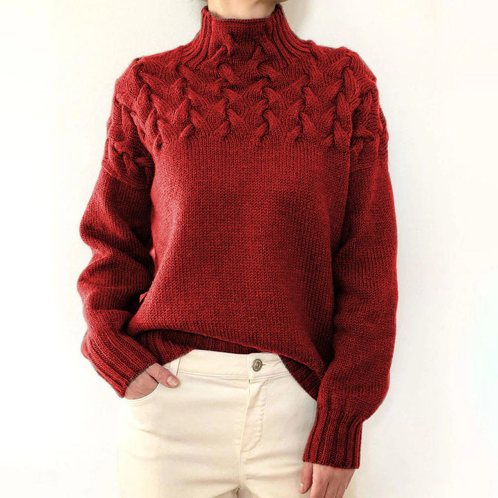 Deep red cable-knit turtleneck jumper with a braided yoke design and ribbed cuffs, worn with cream trousers.