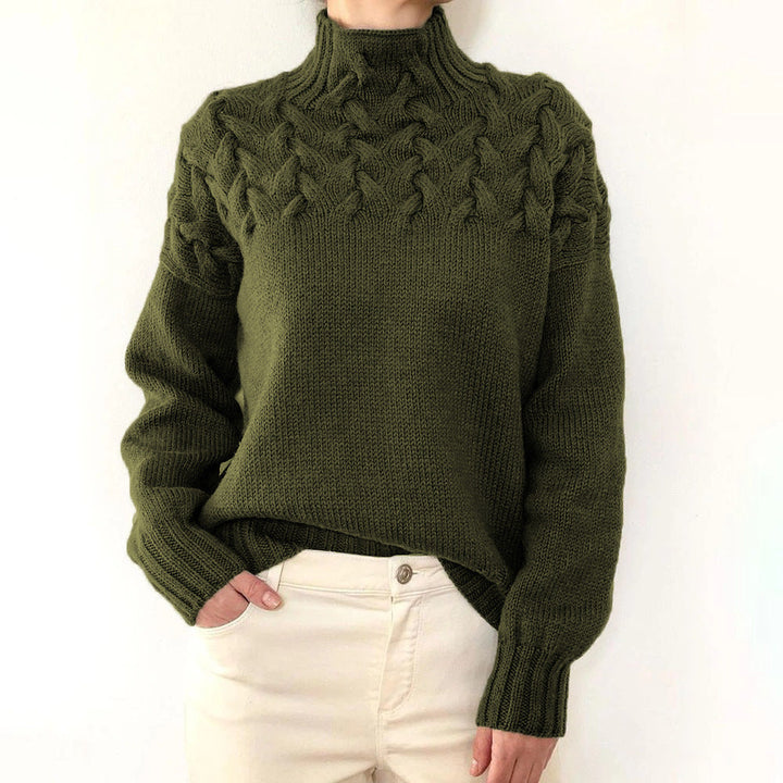 Olive green cable knit turtleneck jumper with a braided yoke design and relaxed fit, styled with cream trousers.