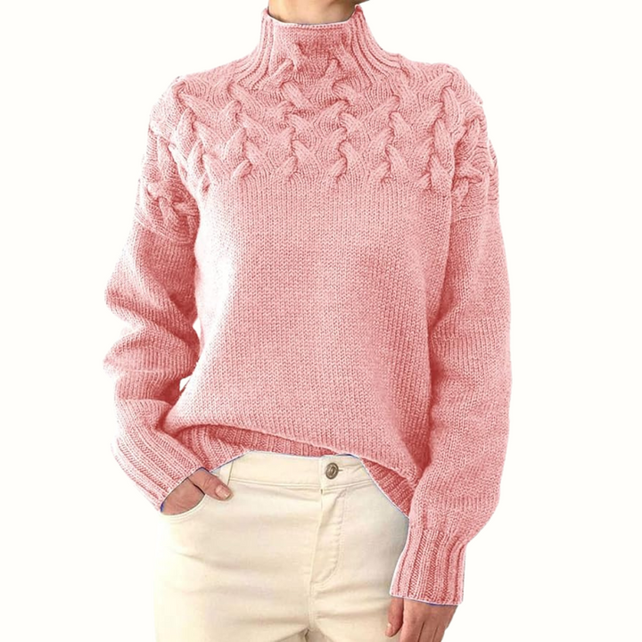 Pink cable knit turtleneck jumper with a braided yoke, relaxed fit, and ribbed cuffs worn with cream trousers.