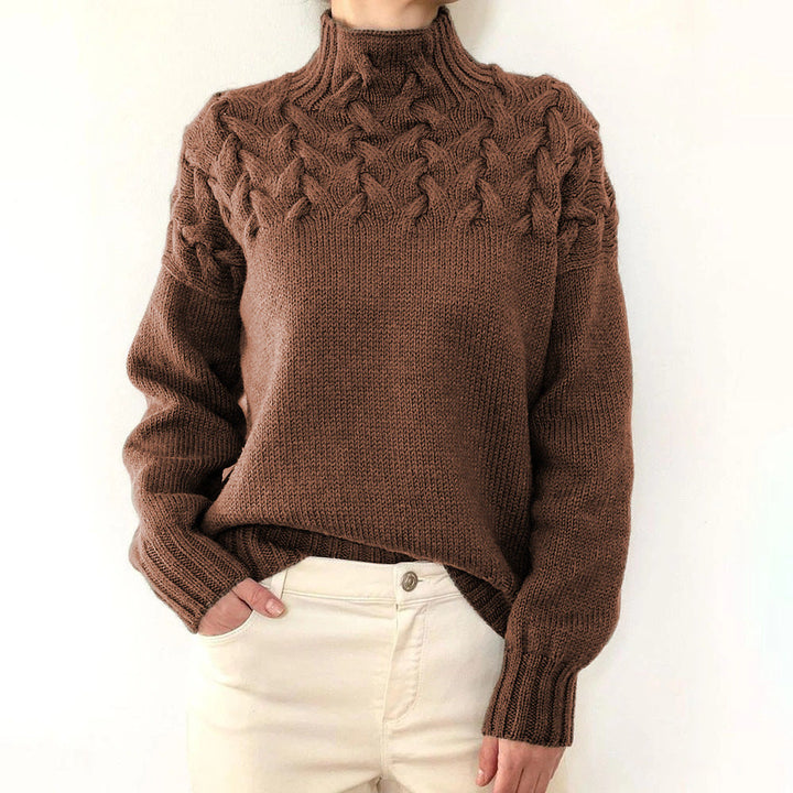 Brown cable knit turtleneck jumper with a braided yoke, relaxed fit, and ribbed cuffs worn with cream trousers.