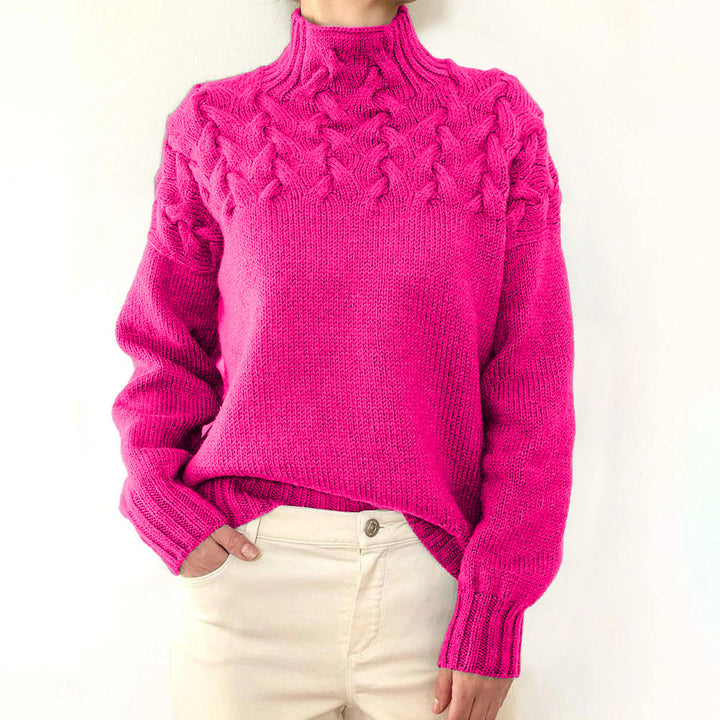 Bright pink cable knit turtleneck jumper with a braided yoke and ribbed cuffs, styled with cream trousers.