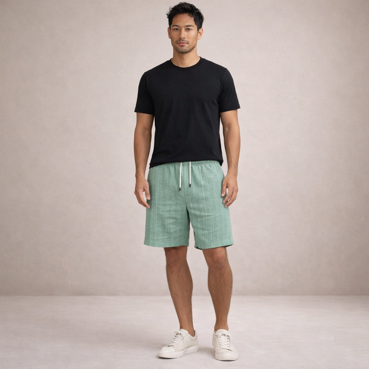 Man wearing sage green linen-look drawstring shorts with a black t-shirt and white sneakers.