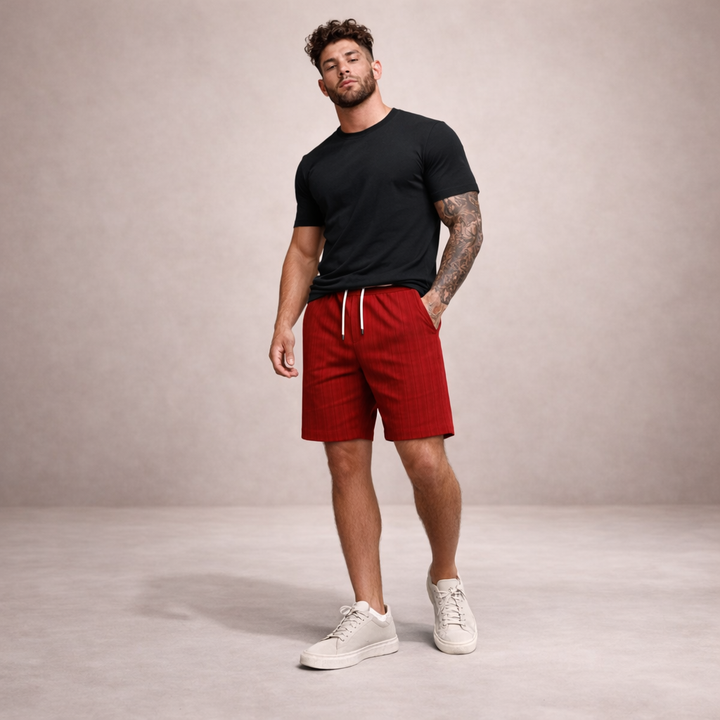 Man wearing red linen-look drawstring shorts with a black t-shirt and white sneakers against a neutral background.