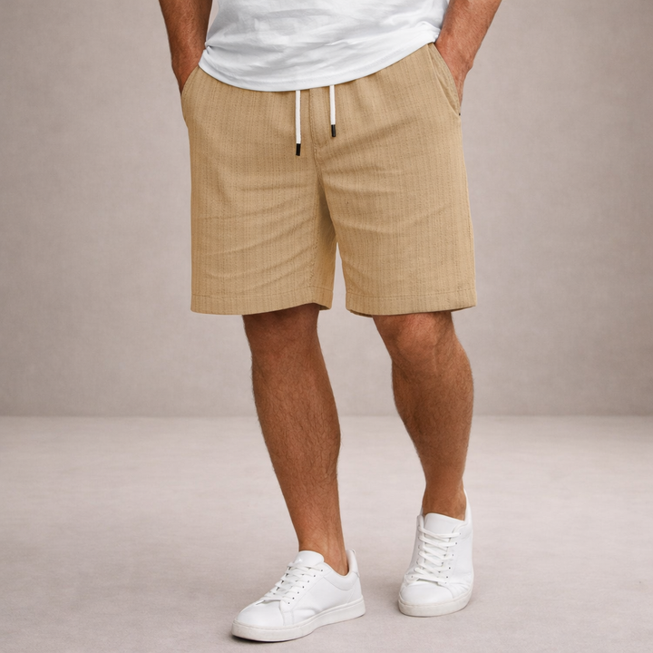 Men's beige linen-look drawstring shorts with a relaxed fit and side pockets, paired with a white t-shirt and sneakers.