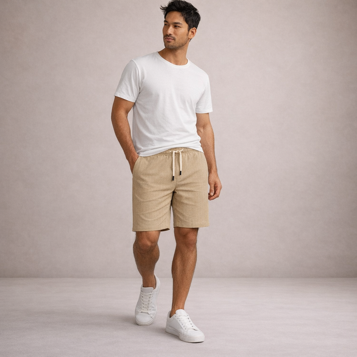 Man wearing beige linen-look drawstring shorts with a white t-shirt and sneakers against a neutral background.