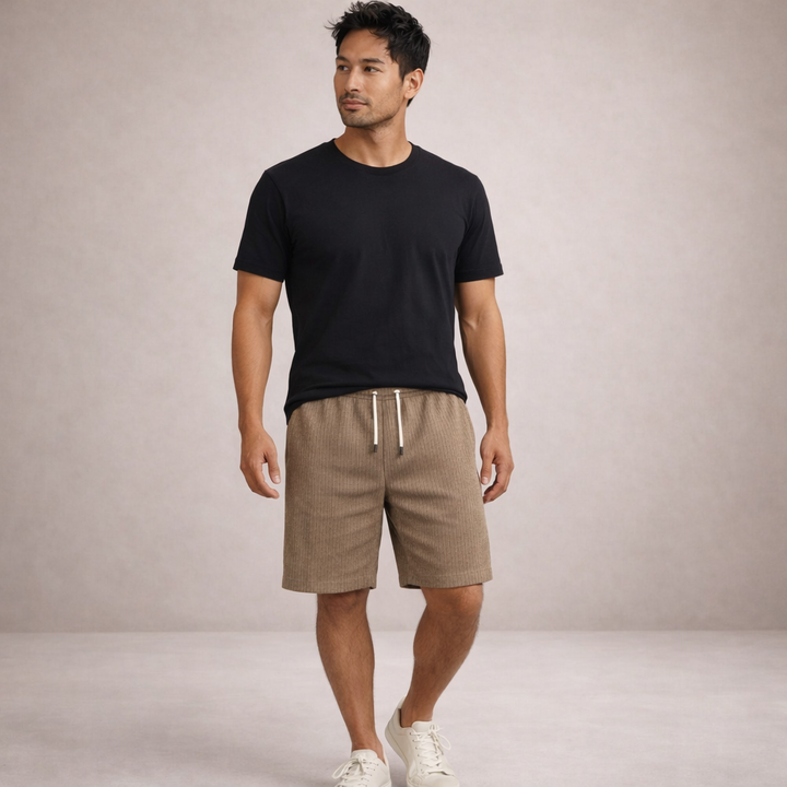 Man wearing beige linen-look drawstring shorts with a black t-shirt and white sneakers against a neutral background.