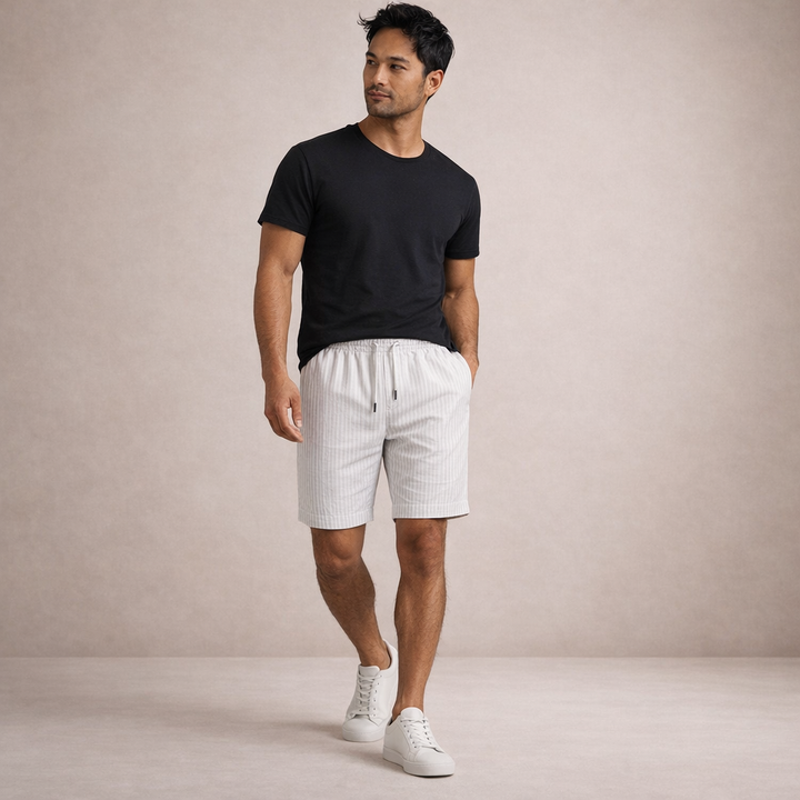 Man wearing white striped linen-look drawstring shorts with a black t-shirt and white sneakers.
