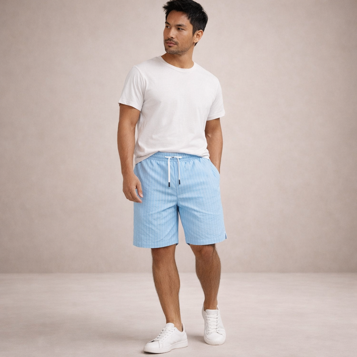 Man wearing light blue pinstriped linen drawstring shorts with a white t-shirt and sneakers.