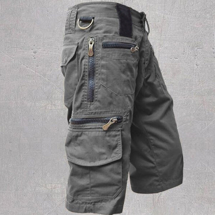 Dark grey cotton cargo shorts featuring multiple zip and flap pockets, a D-ring, and a structured, modern fit.