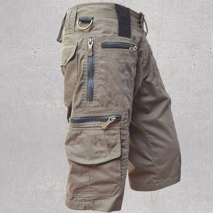 Olive green cotton cargo shorts featuring multiple zip and flap pockets, a D-ring, and a structured, modern fit.