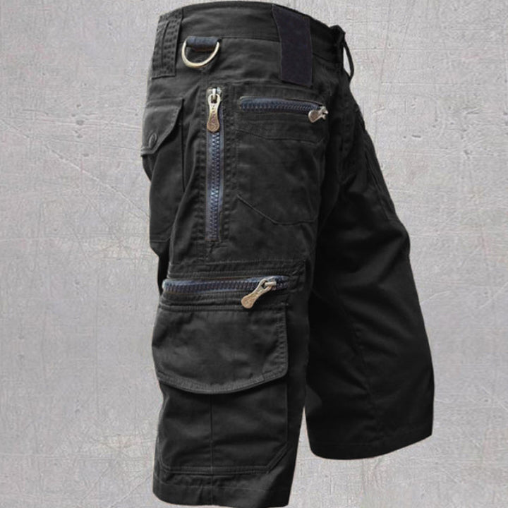 Black cotton cargo shorts featuring multiple zip and flap pockets, a D-ring attachment, and an adjustable drawstring waist.