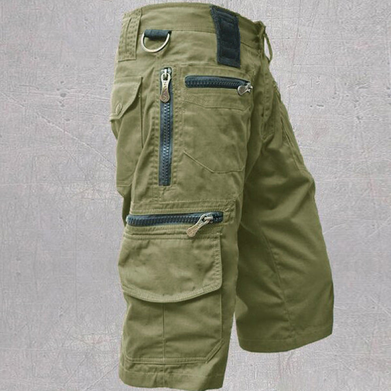 Olive green cotton cargo shorts featuring multiple zip and flap pockets, a D-ring, and a structured, durable utility design.