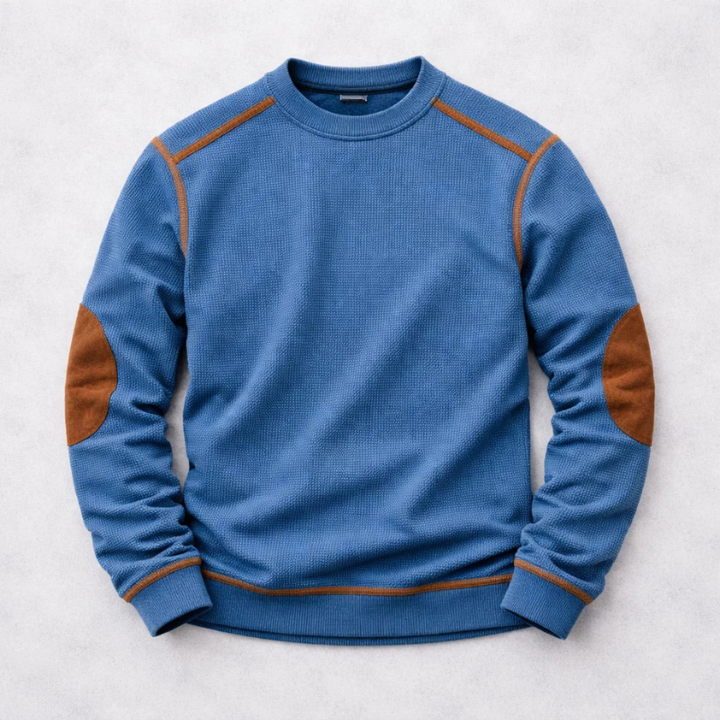 Blue crew neck waffle-knit jumper featuring brown contrast elbow patches and shoulder detailing on a light background.