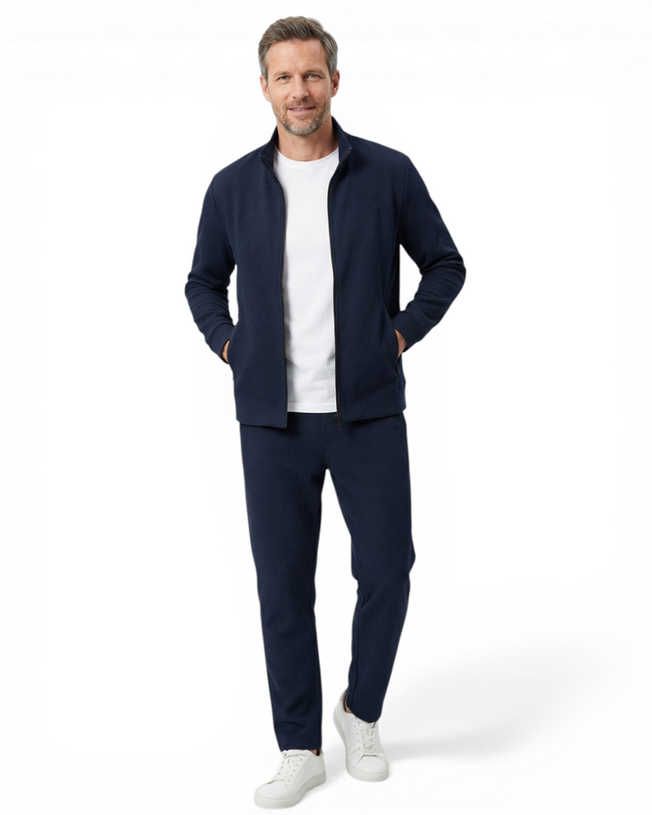 Man wearing a navy blue textured zip-up tracksuit with a funnel neck and matching slim-fit drawstring trousers.