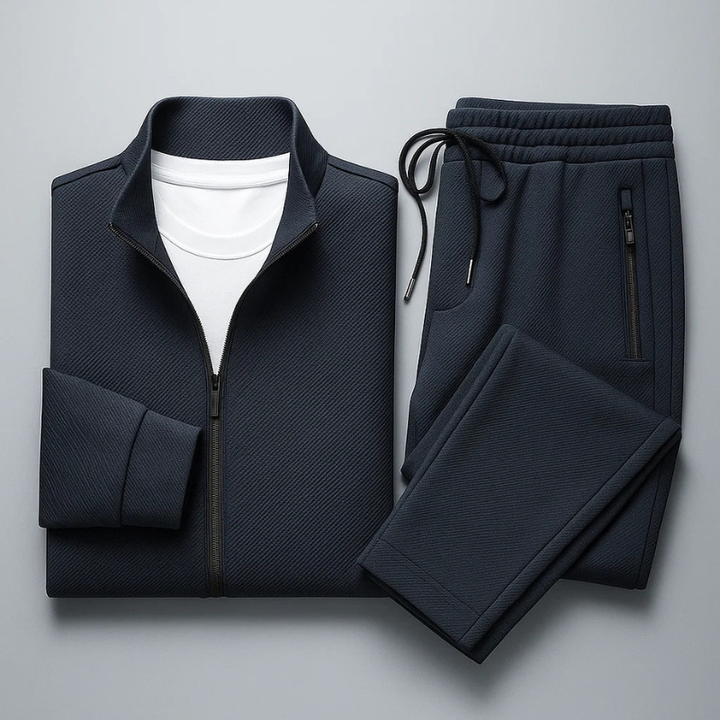 Navy blue textured zip-up tracksuit set with a funnel neck jacket and drawstring trousers on a grey background.