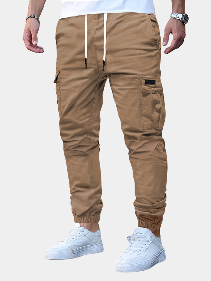 Tan men's cargo joggers with a drawstring waist, side pockets, and elasticated cuffed ankles worn with white trainers.
