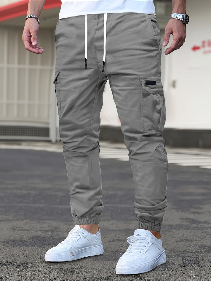 Grey men's cargo joggers with a drawstring waist, side pockets, and cuffed ankles worn with white trainers.