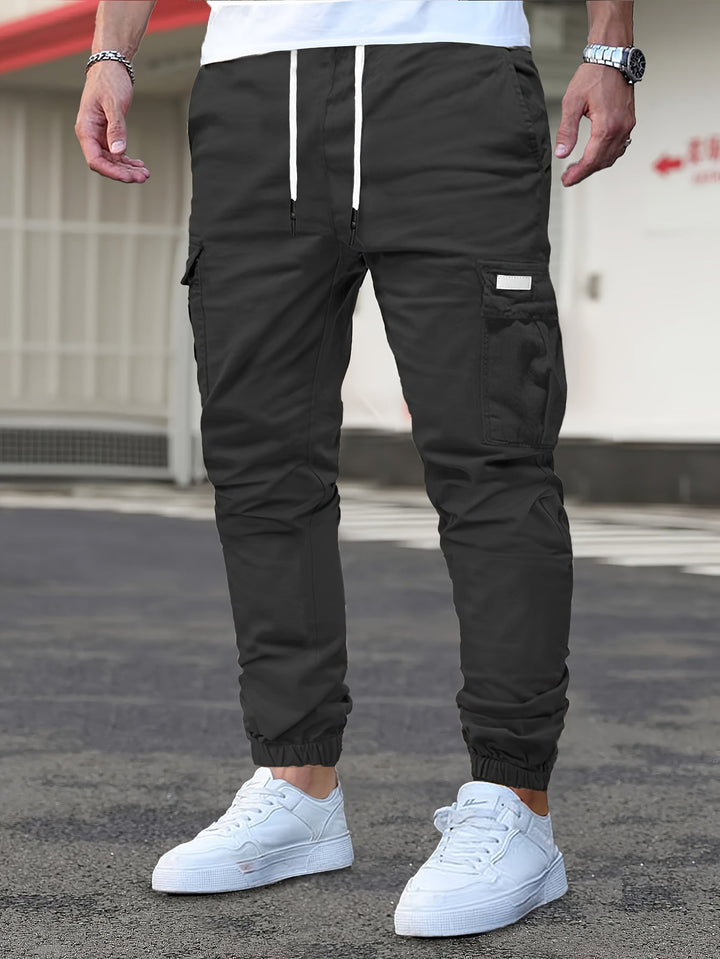 Men's black cargo joggers with a drawstring waist, side pockets, and cuffed ankles, styled with white trainers.