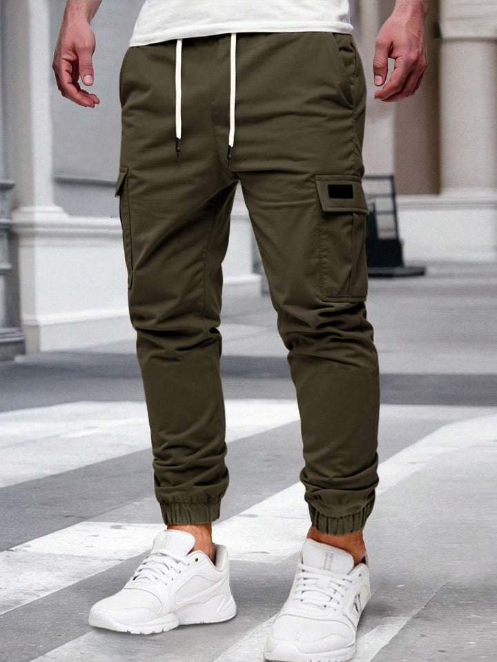 Olive green cargo joggers with a drawstring waist, side pockets, and elasticated cuffed hems worn with white trainers.