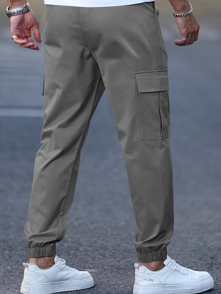 Olive green men's cargo joggers with side pockets, elasticated cuffed ankles, and a tapered fit worn with white trainers.