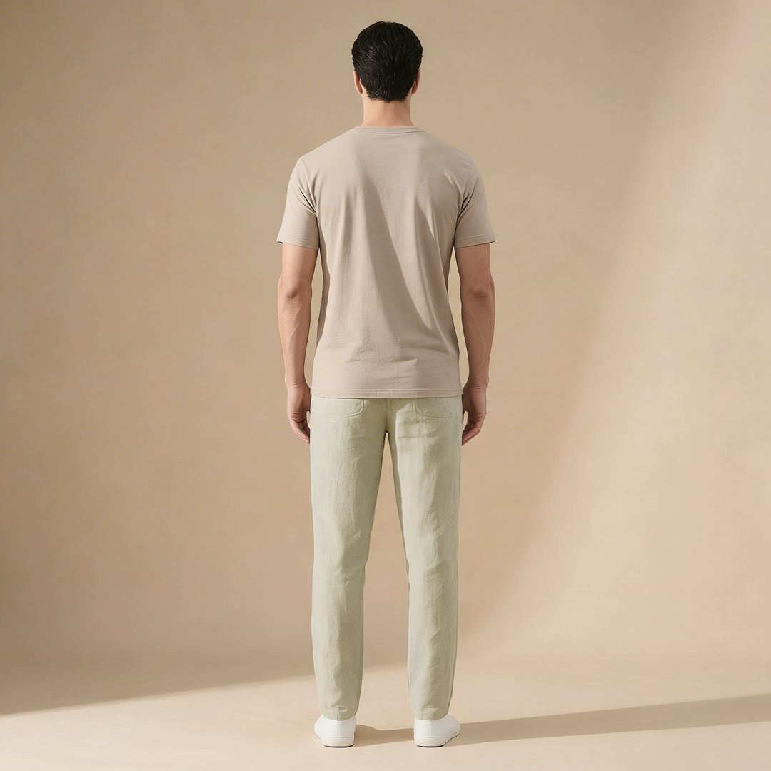 Back view of a man wearing light green straight-leg linen trousers and a beige t-shirt against a neutral background.
