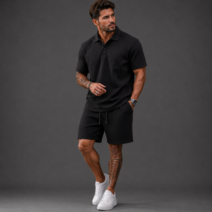 Man wearing a black textured short-sleeve polo shirt and matching drawstring shorts set with white sneakers.