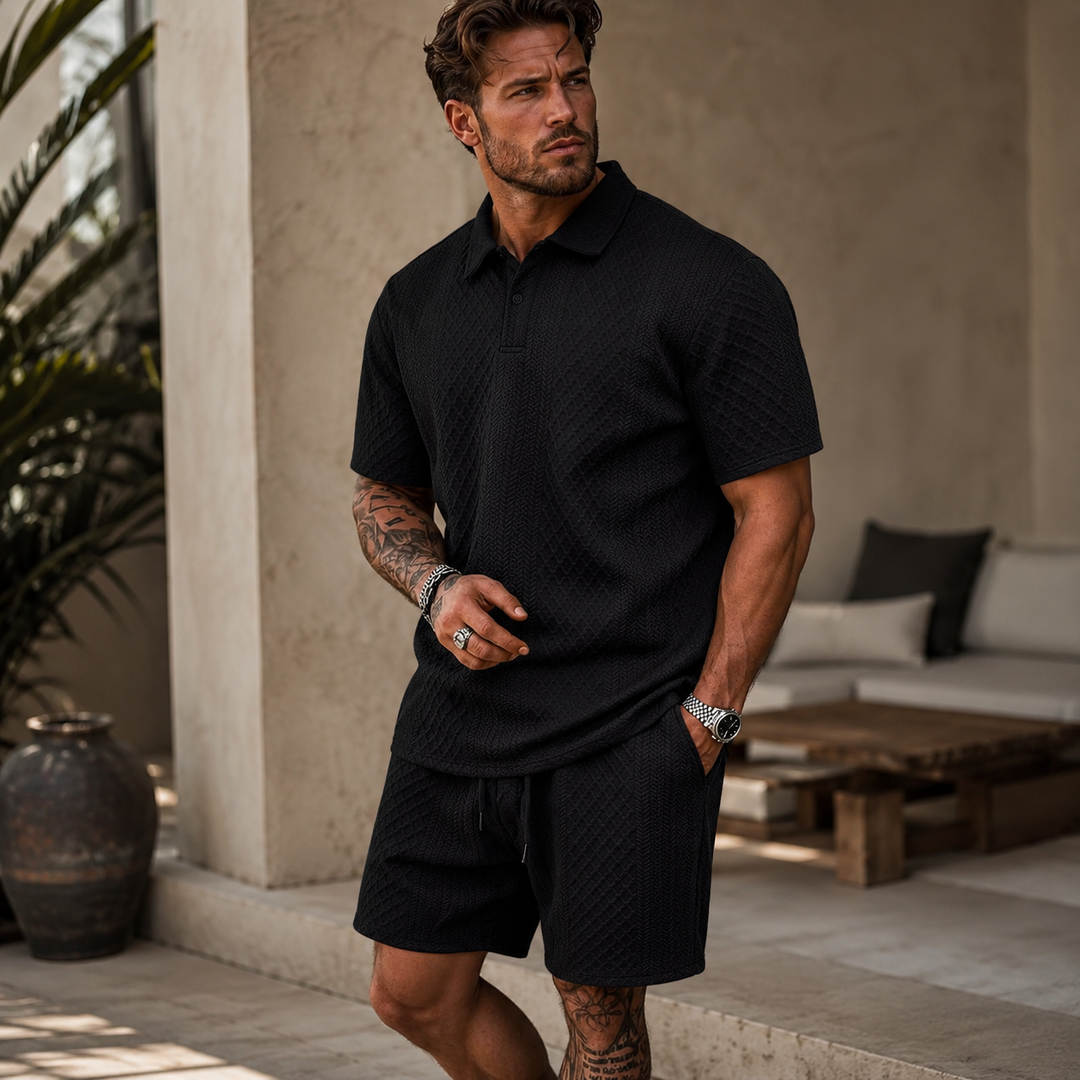 Man wearing a black textured knit polo shirt and matching drawstring shorts in a relaxed summer style.