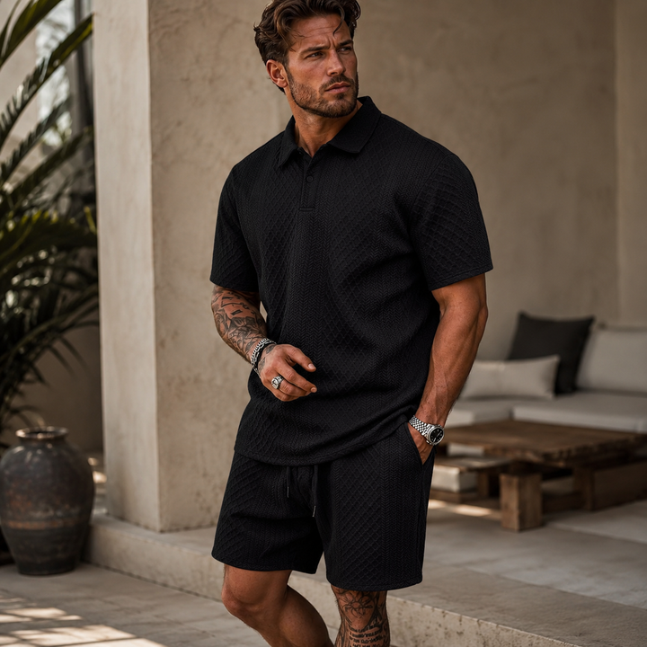 Man wearing a black textured knit polo shirt and matching drawstring shorts in a relaxed summer style.