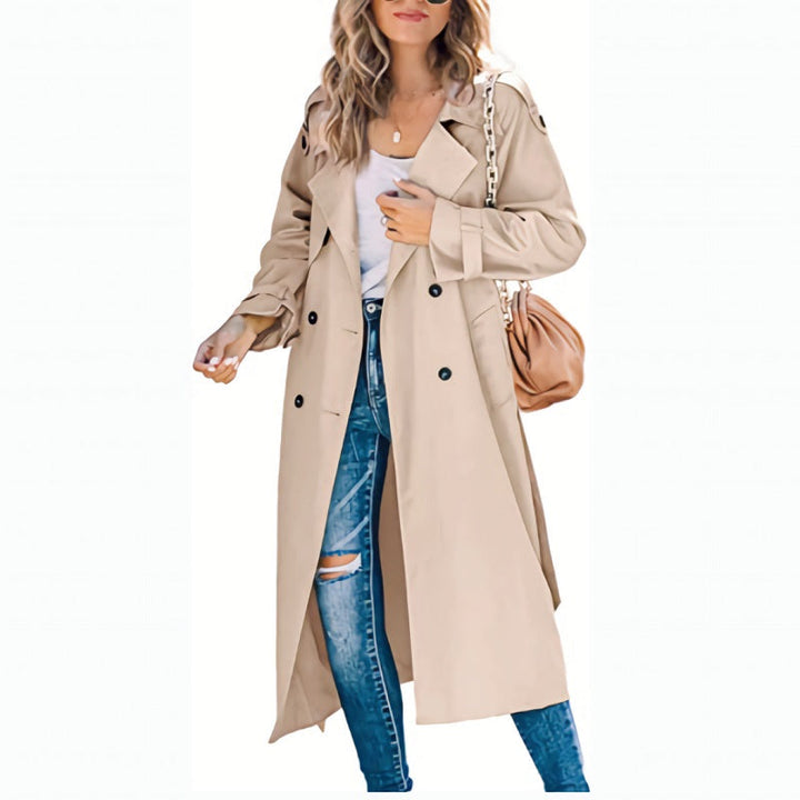 Beige double-breasted long trench coat with notched lapels, styled over distressed blue jeans for a classic mid-season look.