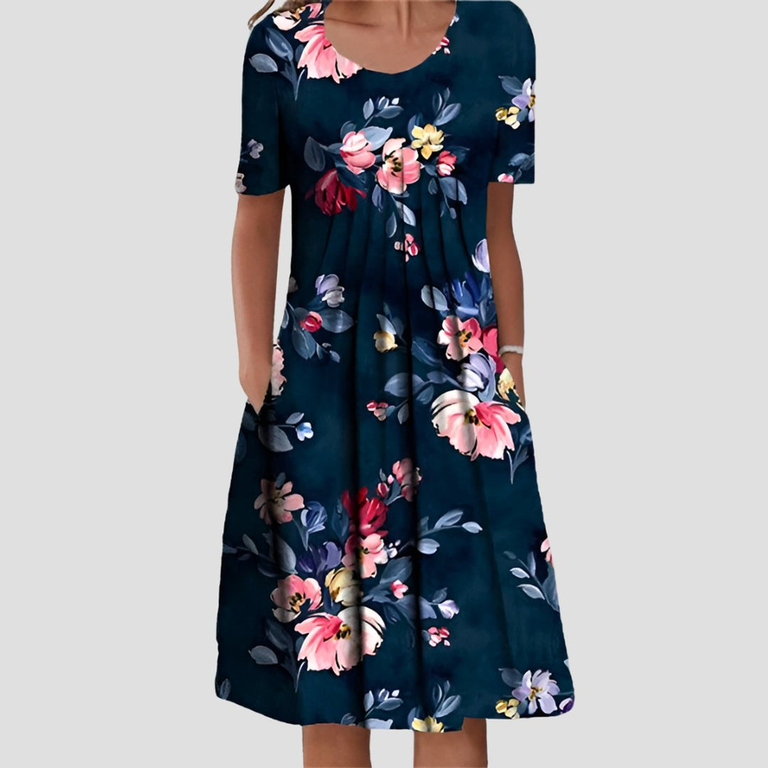 Navy blue A-line midi dress with short sleeves, a pleated bodice, scoop neckline, and vibrant floral print with pockets.