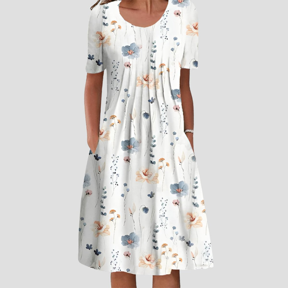 White midi dress with a pleated bodice, short sleeves, scoop neckline, side pockets, and a blue and orange floral print.