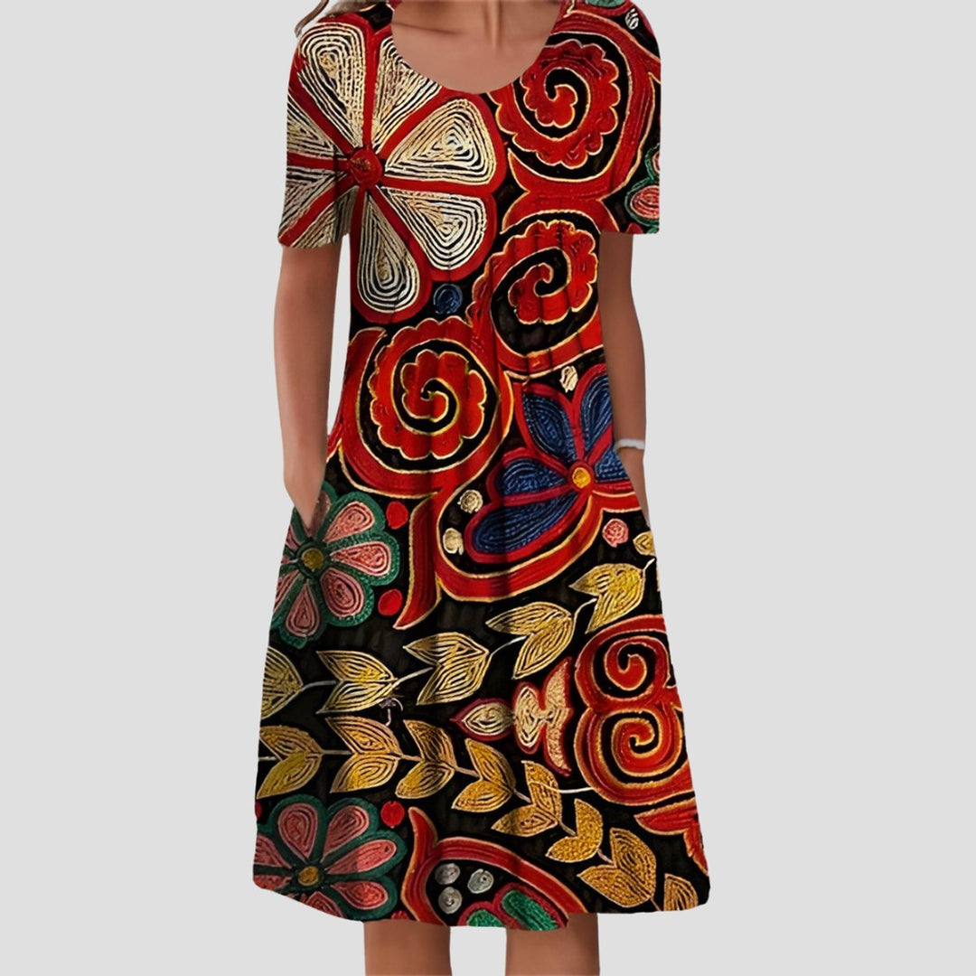 Short sleeve A-line midi dress featuring a vibrant red, gold, and black floral print with a scoop neckline and side pockets.
