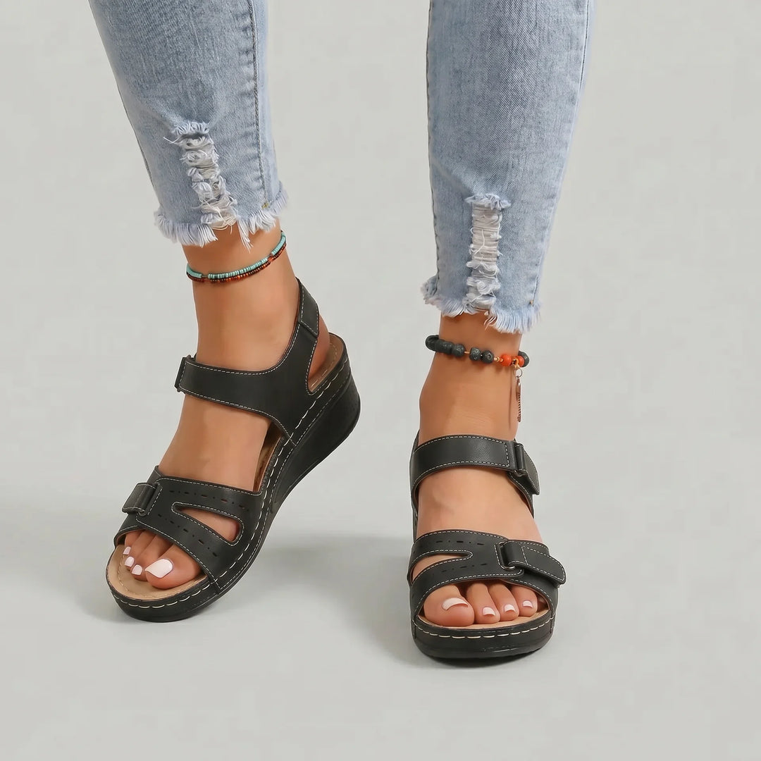 Black sandals worn with light blue jeans on a neutral background