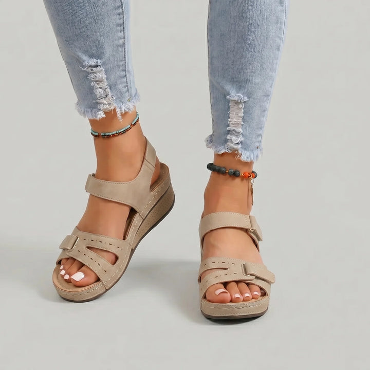 Beige sandals worn with ripped jeans on a plain background