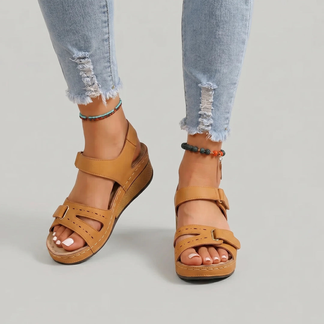 Brown sandals worn with ripped jeans on a neutral background