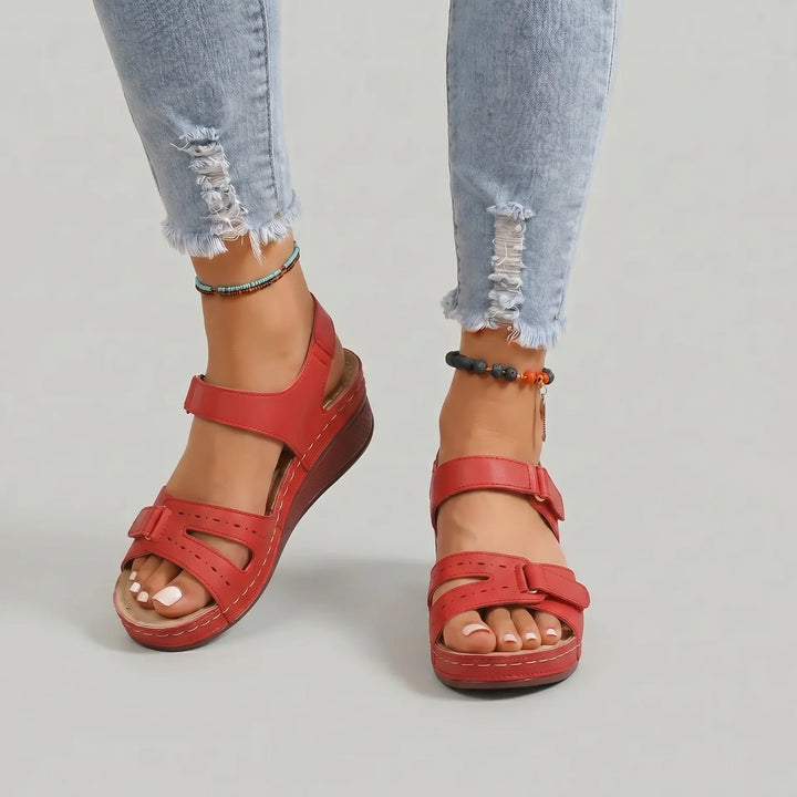 Red sandals worn with ripped jeans on a plain background